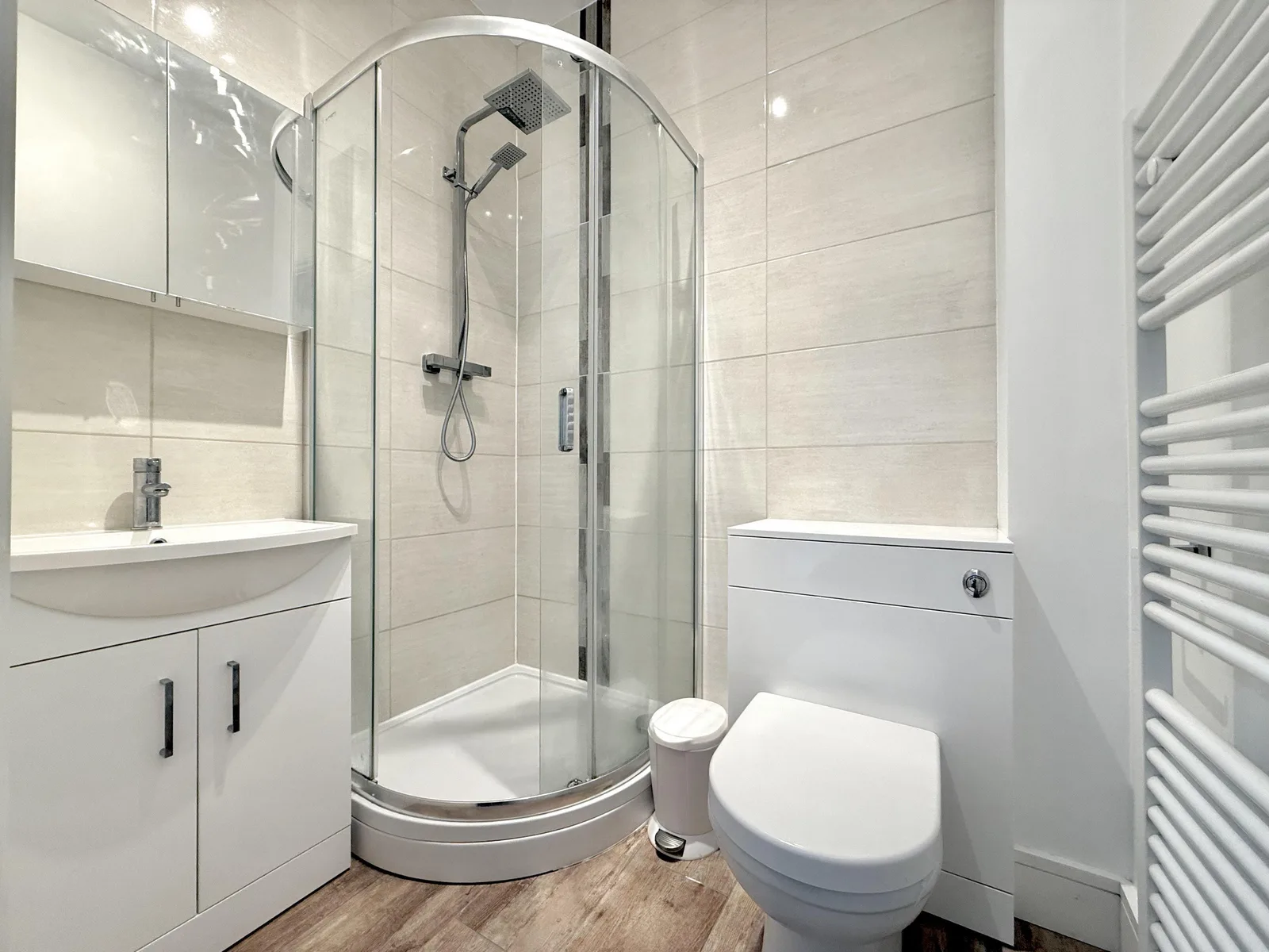 A compact shower room with a quadrant shower enclosure, vanity basin and white heated towel rail